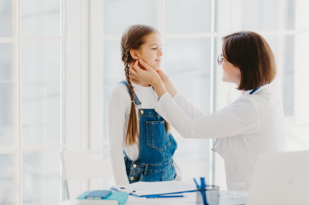 Photo of female pediatrician examines childs throat, being professional skilled pediatrician, consults kid how to prevent tonsillitis, gives good treatment and care. Medical checkup concept.