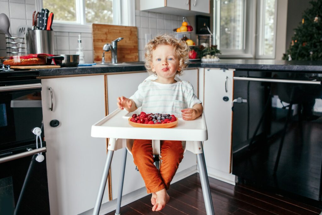 child sitting on baby chair and eating fruits
